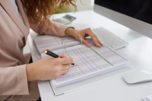 Eine Frau prüft und markiert Finanzdaten am Schreibtisch, passend zur übersichtlichen Haushaltsbuch Vorlage für Einnahmen und Ausgaben.